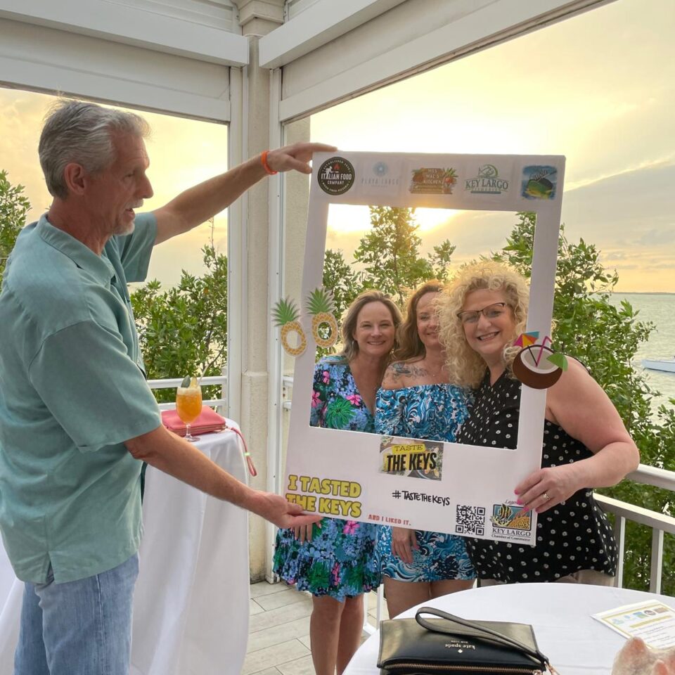 Man holding up a Taste the Keys photo frame for three women