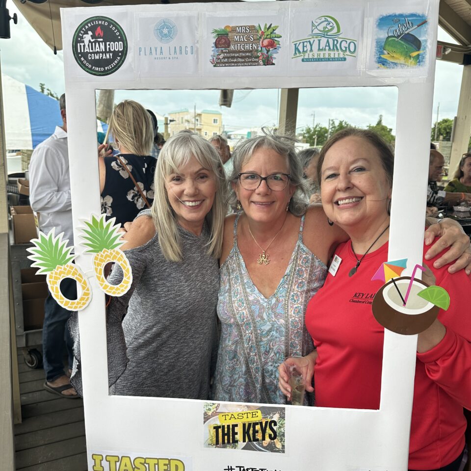 Three women smiling in a Taste the Keys photo frame on a waterfront deck