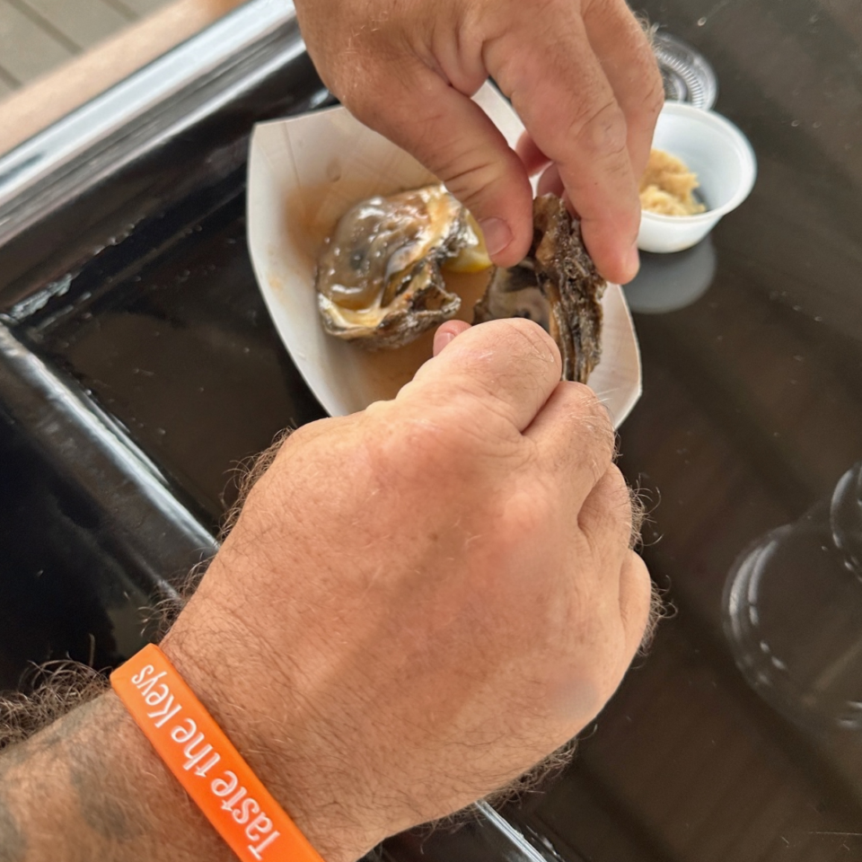 Guest wearing a Taste the Keys wristband shucking an oyster