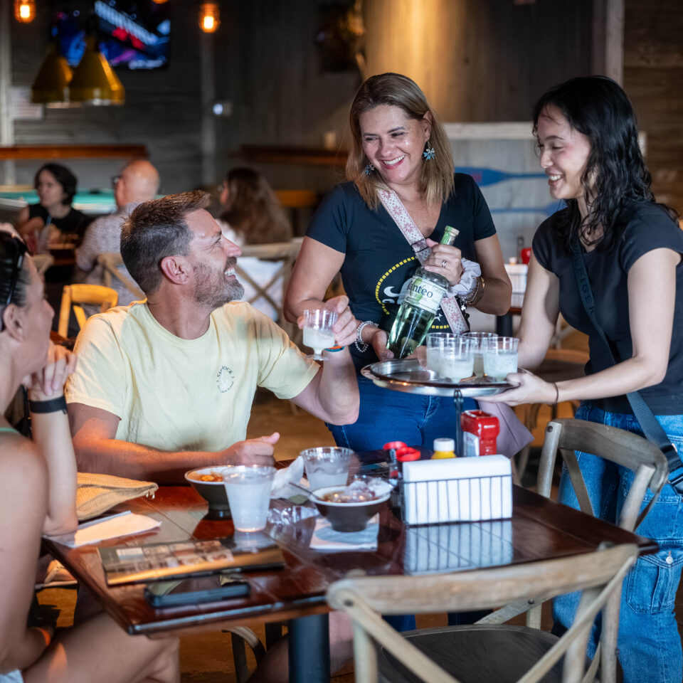 Staff pouring drinks for smiling guests at a restaurant table